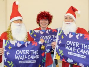 Three Over The Wall Camp staff dressed as Santa and with tinsel holding a flag